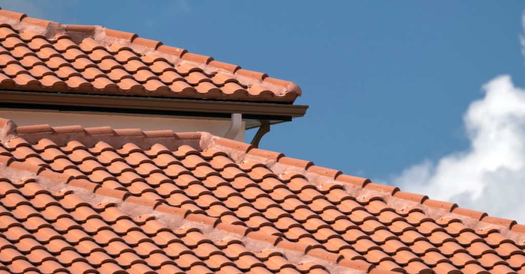 A close-up of the roof of a house covered in overlaid orange clay shingles, with a clear sky in the background.